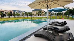 a swimming pool with chairs and an umbrella and a pool at Villa 3PN Novaworld Phan Thiết in Phan Thiet
