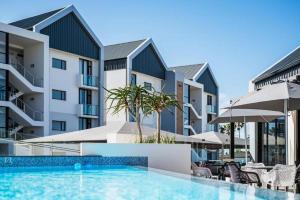a swimming pool with chairs and umbrellas in front of buildings at Bella Mare 12 on Second in Gqeberha