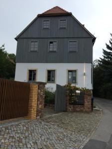 a white house with a black roof and a fence at Ferienwohnung Geißler in Radebeul