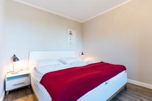 a bedroom with a white bed with a red blanket at Fehmarnstrand 77 Whg 2 in Staberdorf +9 photos