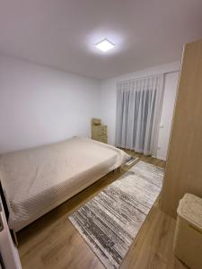a white bedroom with a bed and a rug at Apartament me qera Gjilan,te sheshi in Gjilan