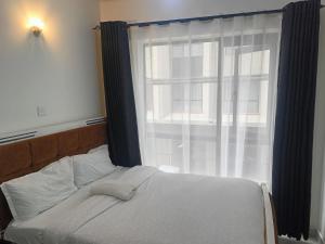 Una cama en un dormitorio con una ventana grande. en Legatus Cozy Studios 1, en Nairobi