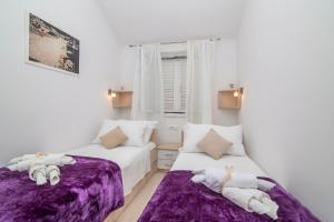 2 Betten in einem weißen Zimmer mit lila Bettwäsche in der Unterkunft Apartment Superb View 2 in Dubrovnik