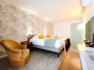 a bedroom with a bed and a chair and a television at Hotel Des Tuileries in Nîmes