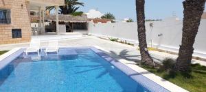 a swimming pool with two chairs next to a house at Villa Alia Kerkennah in Sidi el Moujahed
