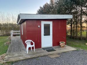 a red shed with a white door and a chair at Bondehytten in Løkken