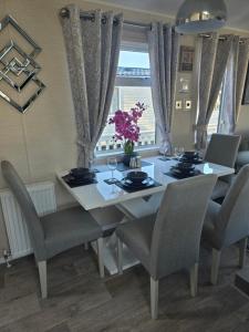 a dining room table and chairs with a white table and flowers at Exclusive Gold 3 Bed Luxury Caravan in Port Seton