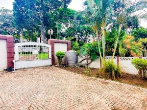 a brick driveway with a white gate and a fence at Tranquil Coastal Home with Pool Family-Friendly Stay in Uvongo Beach