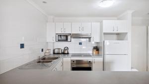 a white kitchen with a sink and a refrigerator at 306 South Pacific Apartments in Port Macquarie