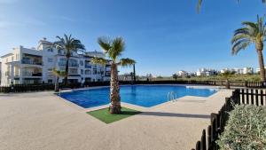 a swimming pool with palm trees in front of a building at Lovely Ground Floor 2 Bed with Golf Course Views in Sucina