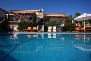 a large swimming pool with chairs and an umbrella at Elies Houses in Agnontas