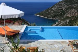 a pool with an umbrella and chairs and the ocean at Elies Houses in Agnontas