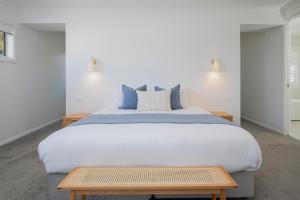 a bedroom with a large white bed with blue pillows at Shoreline Luxe - Refined Beachside Elegance with Spa in Caves Beach