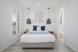 a white bedroom with a large bed with blue pillows at Shoreline Luxe - Refined Beachside Elegance with Spa in Caves Beach