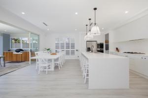 a white kitchen with a table and white chairs at Shoreline Luxe - Refined Beachside Elegance with Spa in Caves Beach
