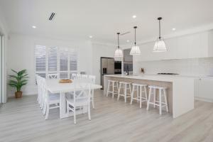 a white kitchen with a white table and chairs at Shoreline Luxe - Refined Beachside Elegance with Spa in Caves Beach