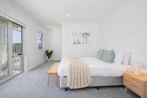 a white bedroom with a bed and a table at Shoreline Luxe - Refined Beachside Elegance with Spa in Caves Beach