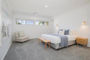 a white bedroom with a bed and a chair at Shoreline Luxe - Refined Beachside Elegance with Spa in Caves Beach