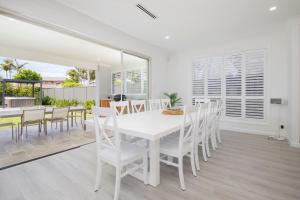 a white dining room with a white table and chairs at Shoreline Luxe - Refined Beachside Elegance with Spa in Caves Beach