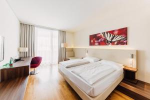 a bedroom with a white bed and a red chair at Hotel Karawankenhof in Villach