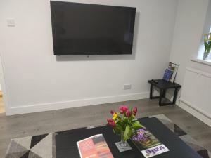 a living room with a tv and a table with flowers at The Caledon in Honeybourne Station