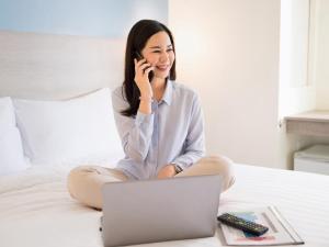 ラノーンにあるHOP INN Ranongの携帯電話で話しながらベッドに座っている女性