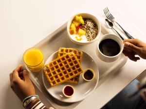 a tray with a plate of waffles and a bowl of fruit at ibis budget Issy Les Moulineaux Paris Ouest in Issy-les-Moulineaux