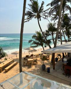 a beach with tables and palm trees and the ocean at Surfing Tusker - Thalpe in Talpe