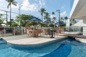 ein Pool mit Tisch, Stühlen und Sonnenschirmen in der Unterkunft Hotel Brisa Praia Pajuçara in Maceió