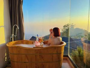 a woman in a wooden bath tub with a window at Mimosa 228-phòng săn mây in Tam Ðảo