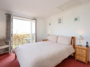 a white bedroom with a bed and a balcony at Seiriol View in Moelfre