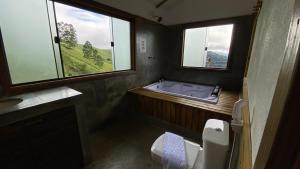 a bathroom with a tub and a toilet and windows at Pousada Verde Serena SFX in São Francisco Xavier