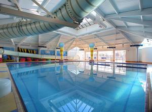 a large swimming pool with blue water in a building at Belinda, Church Farm, Pagham in Pagham