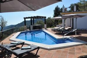 a swimming pool with chairs and an umbrella at Villa El Dorado B&B and Wellness in Cómpeta