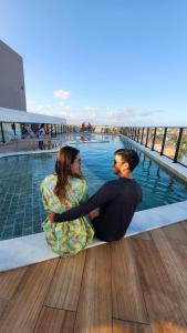 2 personnes assises au bord d'une piscine dans l'établissement Flat 310 Porto City Porto de Galinhas Perto de Tudo, à Porto de Galinhas