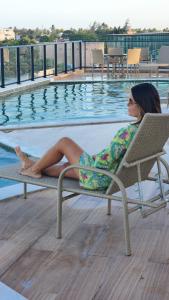 une femme assise sur une chaise à côté d'une piscine dans l'établissement Flat 310 Porto City Porto de Galinhas Perto de Tudo, à Porto de Galinhas 34 autres photos