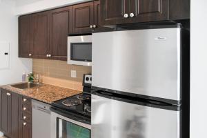 a stainless steel refrigerator in a kitchen with wooden cabinets at Panorama Luxe Suites - Prime Downtown Location in Toronto