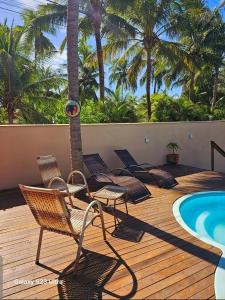 a deck with chairs and a swimming pool with palm trees at Bangalô Suíte Sol do Gostoso in São Miguel do Gostoso