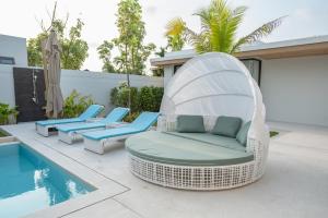 a white wicker chair sitting next to a swimming pool at Mouana Breeze Mai Khao 5-bedroom Pool Villa 9910 in Mai Khao Beach