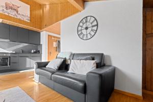 ein schwarzes Ledersofa in einem Wohnzimmer mit einer Uhr an der Wand in der Unterkunft Superbe studio avec une vue magnifique in Leytron + 9 Fotos