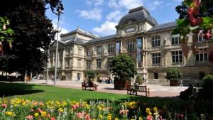 un grand bâtiment en pierre avec bancs dans un parc dans l'établissement L'Oasis Rouennais - Hypercentre - Gare rive Gauche, à Rouen