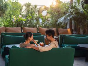 a man and a woman sitting on a green couch at Hotel Sofitel Los Angeles at Beverly Hills in Los Angeles