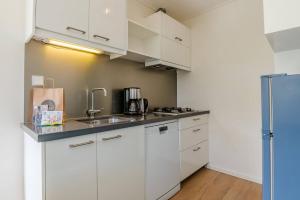 een kleine keuken met witte kasten en een spoelbak bij Hello Zeeland - Appartement Beatrixstraat 27 in Domburg