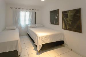 a white bedroom with two beds and a window at Apartamento Economico - AL18 in Maringá +6 photos