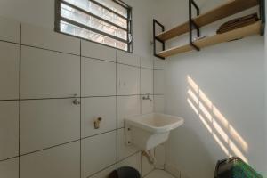 a white bathroom with a sink and a window at Apartamento Economico - AL18 in Maringá