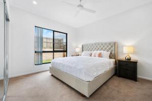 a white bedroom with a large bed and a window at The Crest North Harbour Estate Sleeps 8 in Burpengary East
