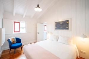 a white bedroom with a bed and a blue chair at Engenho Hostel in Lajes do Pico