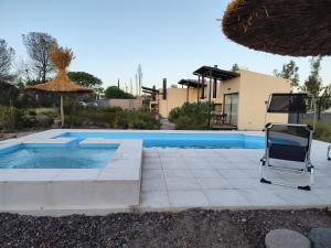 a swimming pool with two chairs and an umbrella at Posada sustentable Los Chañares con vista a la montaña in Ciudad Lujan de Cuyo