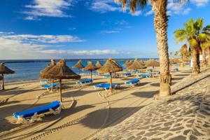 a beach with straw umbrellas and chairs and the ocean at Los Cristianos Penthouse in Arona