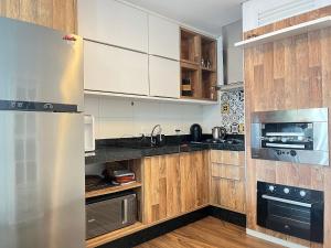 une cuisine avec des armoires en bois et un réfrigérateur en acier inoxydable dans l'établissement Residencial Porto Piçarras - Itacolomi, à Balneário Piçarras